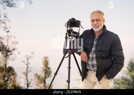 A SENIOR ADULT MAN POSING HAPPILY WITH CAMERA ON HILL TOP Stock Photo