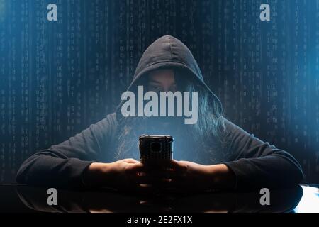 Hacker with cellphone. Young woman using dark web with smartphone. Stock Photo