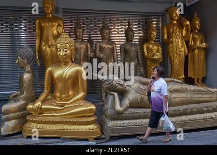 A woman passes Buddha statues placed in front of a factory for Buddha statues and Buddhist religious objects in Bamrung Muang Road, Bangkok, Thailand