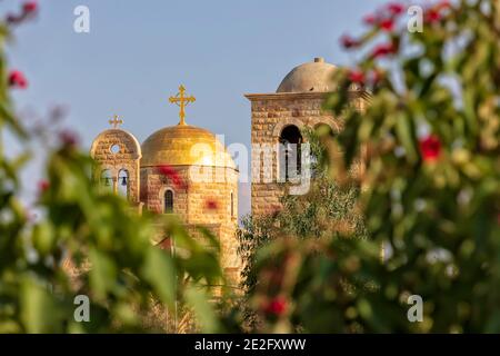 View of the bell tower and golden domes of the Christian church through blurred plants in the foreground Stock Photo