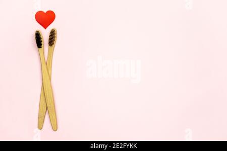 Flat lay composition with heart shape with bamboo toothbrushes and space for text on pink background, top view. Ecology concept with healthy lifestyle Stock Photo