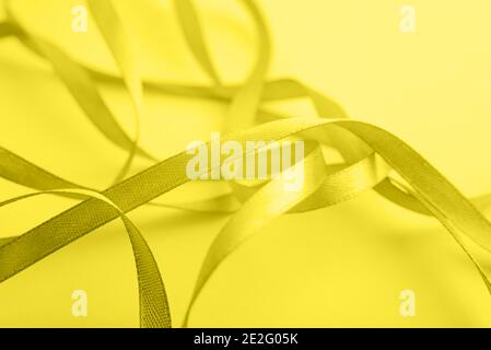 Curved yellow gold silk ribbon on yellow background. Closeup. Trendy color. Color 2021. Stock Photo