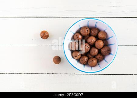 Organic Macadamia nuts (Macadamia integrifolia) in shell on wooden white table. Top view, overhead, copy space Stock Photo