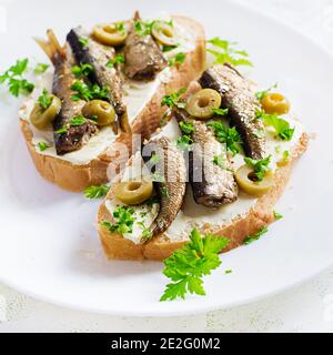 Sandwich - smorrebrod with sprats, green olives and butter on light table. Danish cuisine. Stock Photo