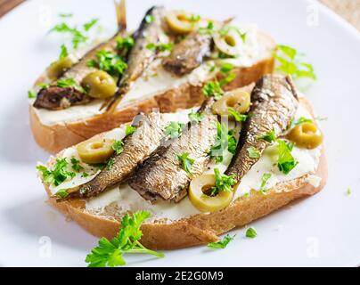 Sandwich - smorrebrod with sprats, green olives and butter on wooden table. Danish cuisine. Stock Photo