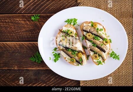 Sandwich - smorrebrod with sprats, green olives and butter on wooden table. Danish cuisine. Top view, overhead, flat lay Stock Photo
