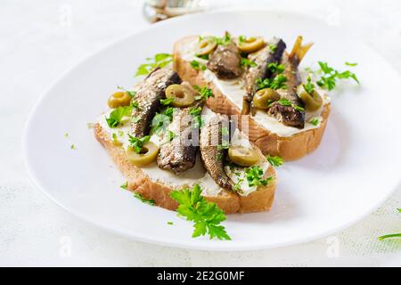 Sandwich - smorrebrod with sprats, green olives and butter on light table. Danish cuisine. Stock Photo