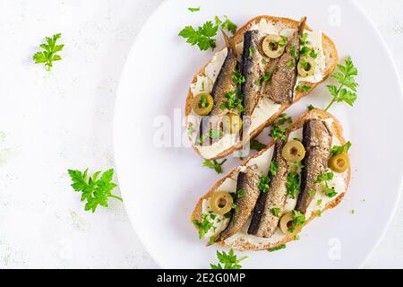 Sandwich - smorrebrod with sprats, green olives and butter on light table. Danish cuisine. Top view, overhead, flat lay Stock Photo