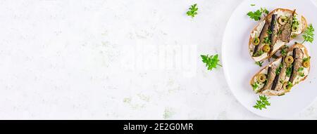 Sandwich - smorrebrod with sprats, green olives and butter on light table. Danish cuisine. Top view, overhead, banner Stock Photo