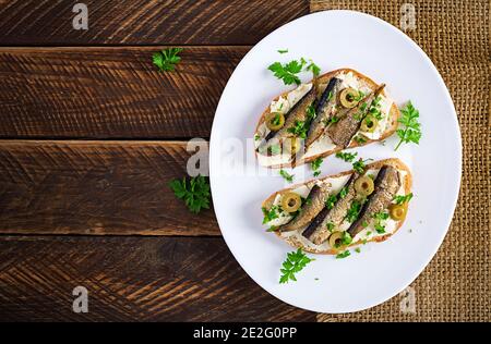 Sandwich - smorrebrod with sprats, green olives and butter on wooden table. Danish cuisine. Top view, overhead, flat lay Stock Photo