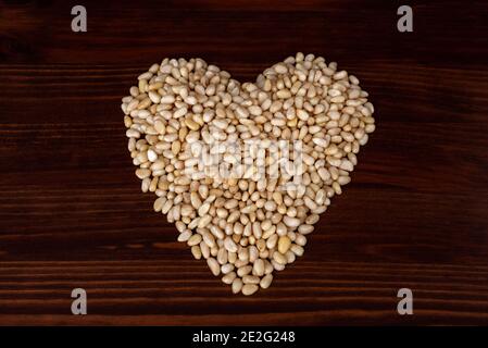 Pine nuts forming a heart shape on dark vintage wooden table. Top view or flat lay Stock Photo