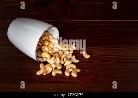 Scattered cashew in a bowl against dark rustic wooden background. Cashew nuts Stock Photo