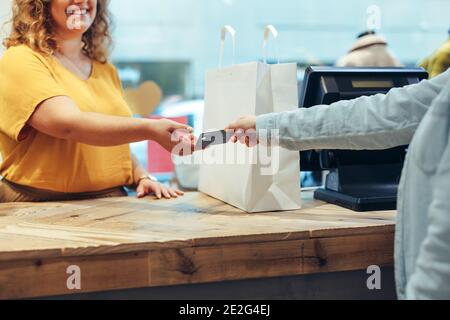 Female customer handing over her credit card to the cashier at clothing store. Shopper paying of her purchases with credit card. Stock Photo