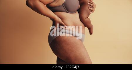 Mid section of plus size woman with baby. Body positive woman postpartum. Mother with visible postpartum body marks with baby. Stock Photo