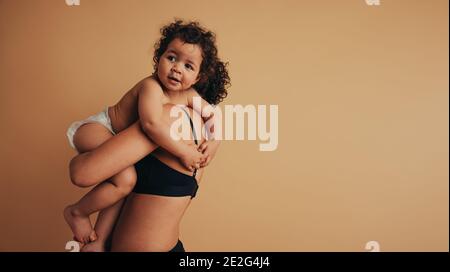 Cute infant in mothers arms. Mother carrying her baby on brown background. Stock Photo