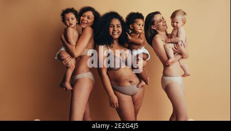Group of mothers with babies. Women with postpartum bodies carrying their children looking at camera and smiling. Stock Photo