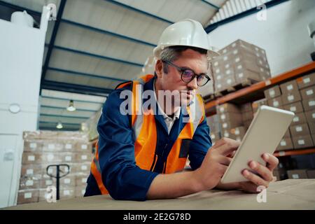 Male factory engineer wearing spectacles using digital tablet leaning on table Stock Photo