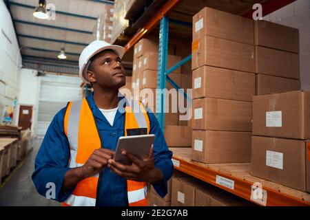 African male supervisor checking product or parcel goods on shelf pallet in industry storage warehouse using digital tablet Stock Photo