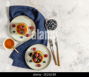 Two plates with tasty american pancakes with raspberries, blueberries, and honey. Top view, marble table. Stock Photo