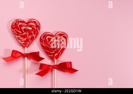Sweet red lollipops hearts with ribbon on pastel pink as valentines day background. Stock Photo