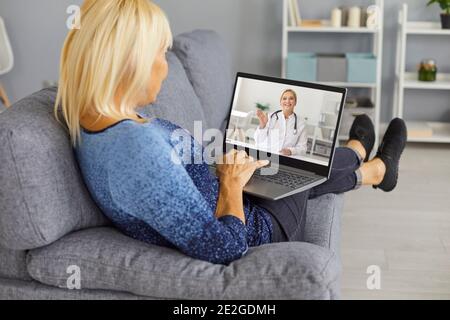 Woman lying on sofa and communicating with smiling woman therapist online on laptop Stock Photo