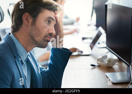 Young tired, ill, overworked business man in formal wear sitting in front of computer Stock Photo