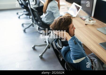 Young tired, ill, overworked business man in formal wear sitting in front of computer Stock Photo