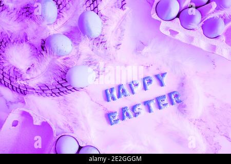 Creative bright composition with festive atmosphere. Easter holiday decorations on marble background. Fluffy white feathers and painted purple eggs in Stock Photo