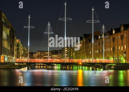 Eliasson Cirkelbroen (Five Circles Pedestrian Bridge) across a canal illuminated at night in a modern residential area with on water light reflection Stock Photo