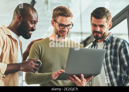 Three cheerful guys watching something on laptop screen Stock Photo