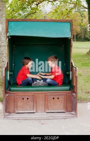 Two kids, brothers,sitting in a sheltered bench, playing hand clapping game, outdoors in the summer Stock Photo