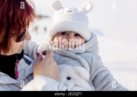 Grandmother holding little toddler boy outdoor on a snowy winter day, having their portrait taken Stock Photo