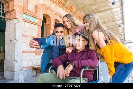 Group of friends take a family member in a wheelchair for a walk in the park on a sunny day Stock Photo