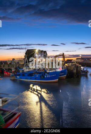 Fishing vessels in Whitstable harbour illuminated at dusk on the North Kent coast. Stock Photo