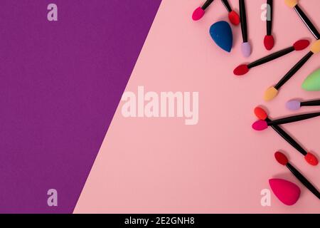 Top view beautiful multicolored bright eyeshadow brushes, face sponges on pink and purple two tone background with copy space, closeup Stock Photo