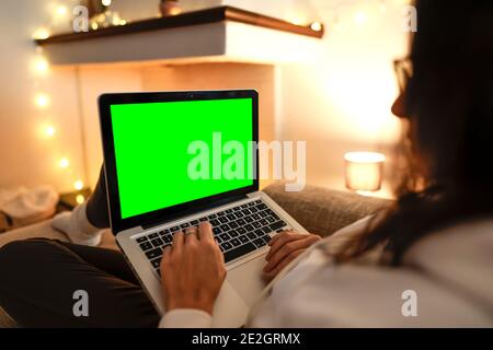 Working from home to change your life: side view close up of young female internet freelance using laptop with blank green screen display comfortably Stock Photo