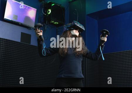 Smiling young woman in VR glasses is gaming using joystick in virtual reality game club. Modern entertainment and leisure concept Stock Photo