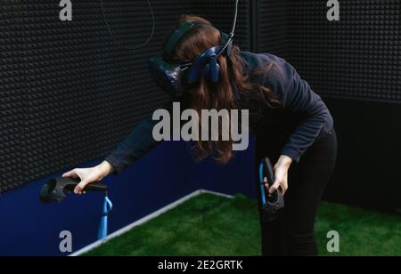 Contemporary woman in virtual reality headset using joystick while playing video game in vr game club. Stock Photo