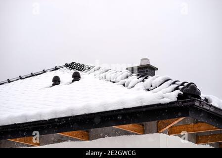 The roof of a single-family house is covered with snow against a cloudy sky, visible ridge tile, system chimney and ceramic ventilation fireplace on t Stock Photo