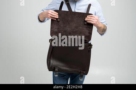 Details of open brown men's shoulder leather bag for a documents and laptop on the shoulders of a man in a blue shirt and jeans with a white Stock Photo