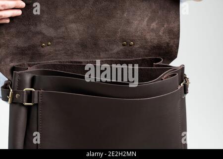 Details of open brown men's shoulder leather bag for a documents and laptop on the shoulders of a man in a blue shirt and jeans with a white Stock Photo