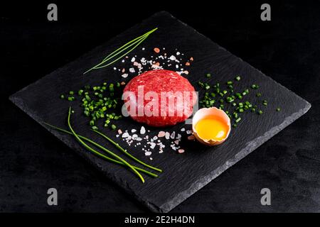 Beef tartar with egg served on a black stone plate. Tartar on a black plate with herbs, salt and chicken yolk. Raw tartare meat.Black background. Top Stock Photo