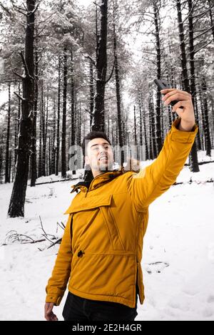 Young man taking a selfie on a snowy forest with a yellow anorak Stock Photo