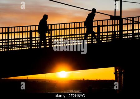 Two people walking silhouetted with bright sunset behind them Stock Photo