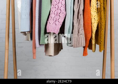 Knitted sweaters on wooden hanger rack on white background Stock Photo