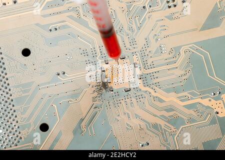 printed circuit board with contact paths and syringe with needle filled with red liquid, concept on theme of cospirology of vaccination and chipizatio Stock Photo