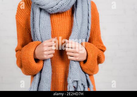 Cropped view of woman in orange knitted sweater and grey scarf on white background Stock Photo