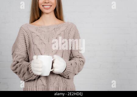 Cropped view of smiling woman in knitted sweater and gloves holding cup on white background Stock Photo