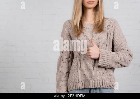 Cropped view of young woman in knitted sweater showing like on white background Stock Photo
