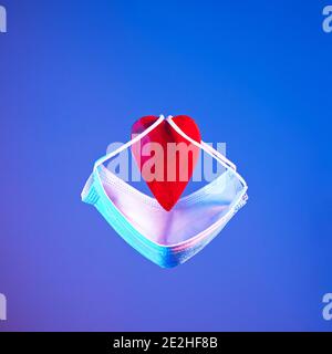 Red heart with a protective mask in neon light. Valentine's Day concept Stock Photo
